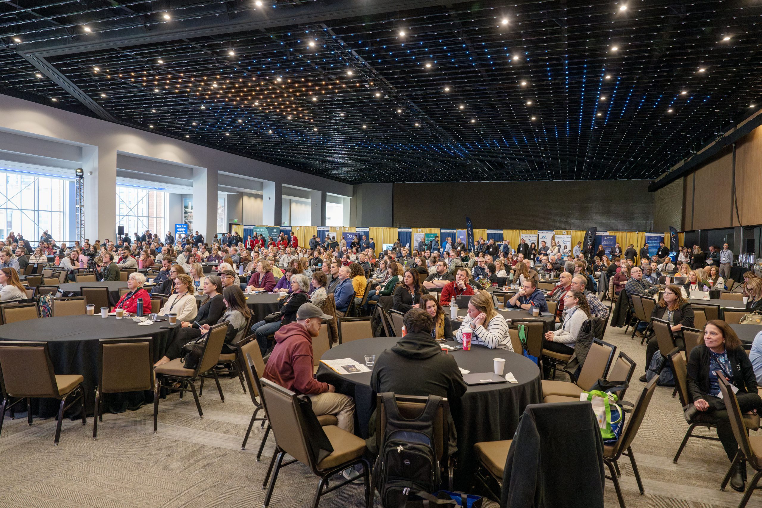 People are seated at conference room tables in a very large room