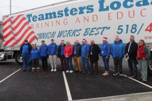SELFI Program students and staff wearing their blue CRB BOCES shirts and Santa hats, take a photo in front of a large white Teamsters truck. 