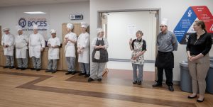 Culinary students stand in a line with their teachers. The students are wearing traditional white culinary garb.