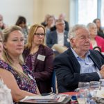 People seated at tables listen to a speaker.