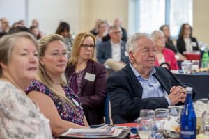 People seated at tables listen to a speaker.