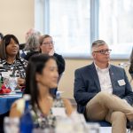 People are seated at tables listening to a speaker.