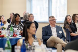 People are seated at tables listening to a speaker.