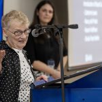 A woman speaking at a podium into a microphone gestures