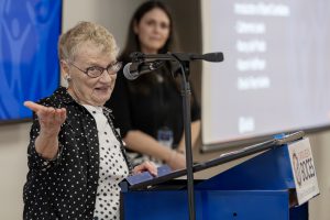 A woman speaking at a podium into a microphone gestures