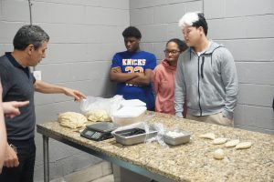 A photo of three students from Guilderland High School and Tuscan Bakery owner Nurettin Ulukay as he demonstrate a baking technique.