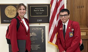 2 students pose by sign