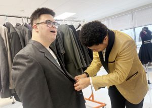 Student helps another with a suit jacket 