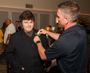 A photo of Capital Region BOCES School Resource Officer assisting a student with putting on his boutonniere.
