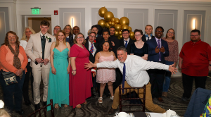 A fun group photos of students and staff as they pose in front of a golden balloon garland at the 2026 Special Education division prom.