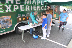 Two young students sample maple syrup from Bittersweet Maple Farm.