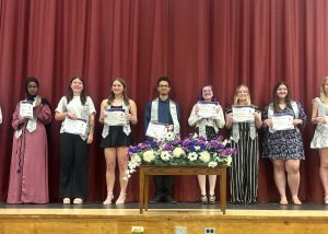 Group of kids pose with certificates behind floral bouquet