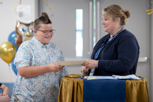A young male student excitedly takes his moving-up certificate from his teacher as she smiles at him. The ceremony took place at Airline Drive Academy.