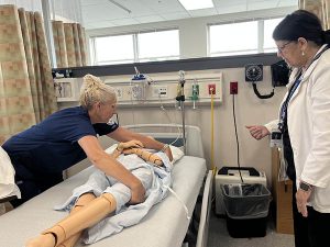Student places a blanket on a patient as the teacher watches