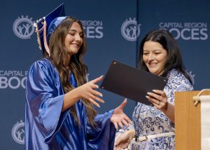 Student and teacher smile while exchanging diploma