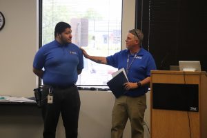 Wearing their royal blue SELFI Program t-shirts, teacher Brent Pierce and graduate Kayin Wethers are photographed together. Brent has his hand on Kayin's shoulder as he presents Kayin with a graduation certificate.