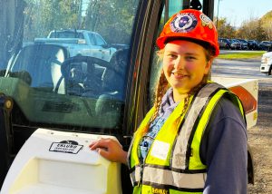 Student poses next to tractor with hard hat on