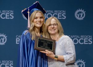 Student and teacher smile while holding award
