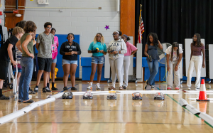 A group of middle school students stand together in the gym as they prepare to test drive the miniature race cars they built.