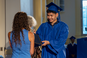 A male student accepts his adult education graduation certificate on stage as he smiles.