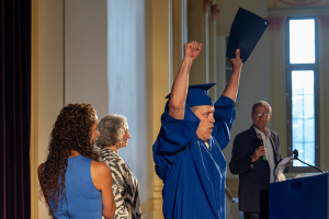 A graduate of the adult education program raises his hands in the air while holding his graduation certificate in one hand.
