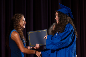 Capital Region BOCES Assistant District Superintended hands a graduation certificate to a female student at the adult education graduation. Both people ae smiling.