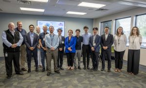 A group of people are photographed in a conference room, they are standing in a line