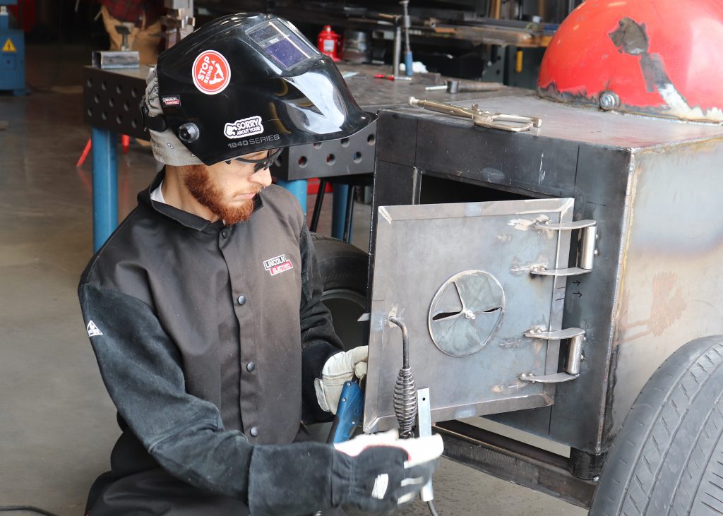 Adult in a welding helmet inspecting a weld