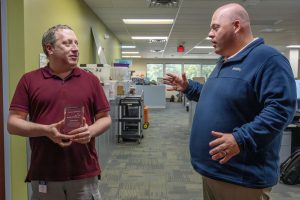 Two men are talking to each other. The one on the right is gesturing, the one on the left is holding an award