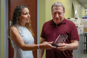 Two people are standing next to each other. One is holding an award, both are looking at it
