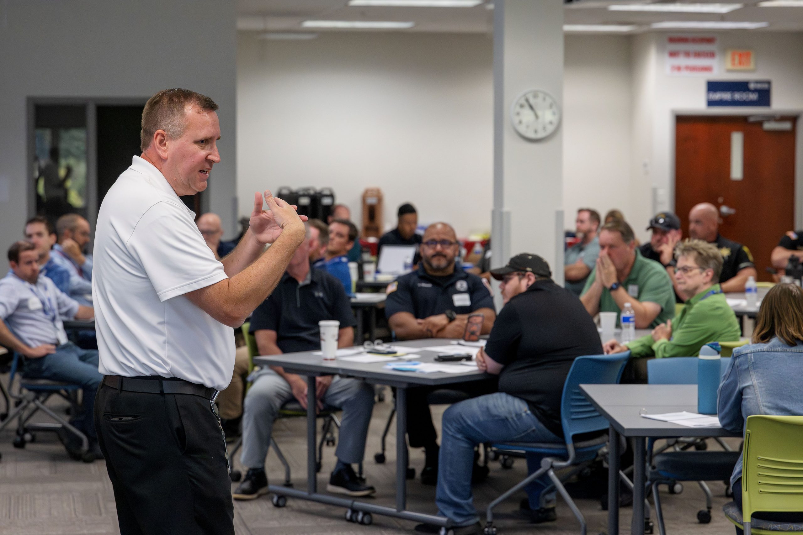 A man is speaking to a conference room full of people who are seated at tables. He is gesturing