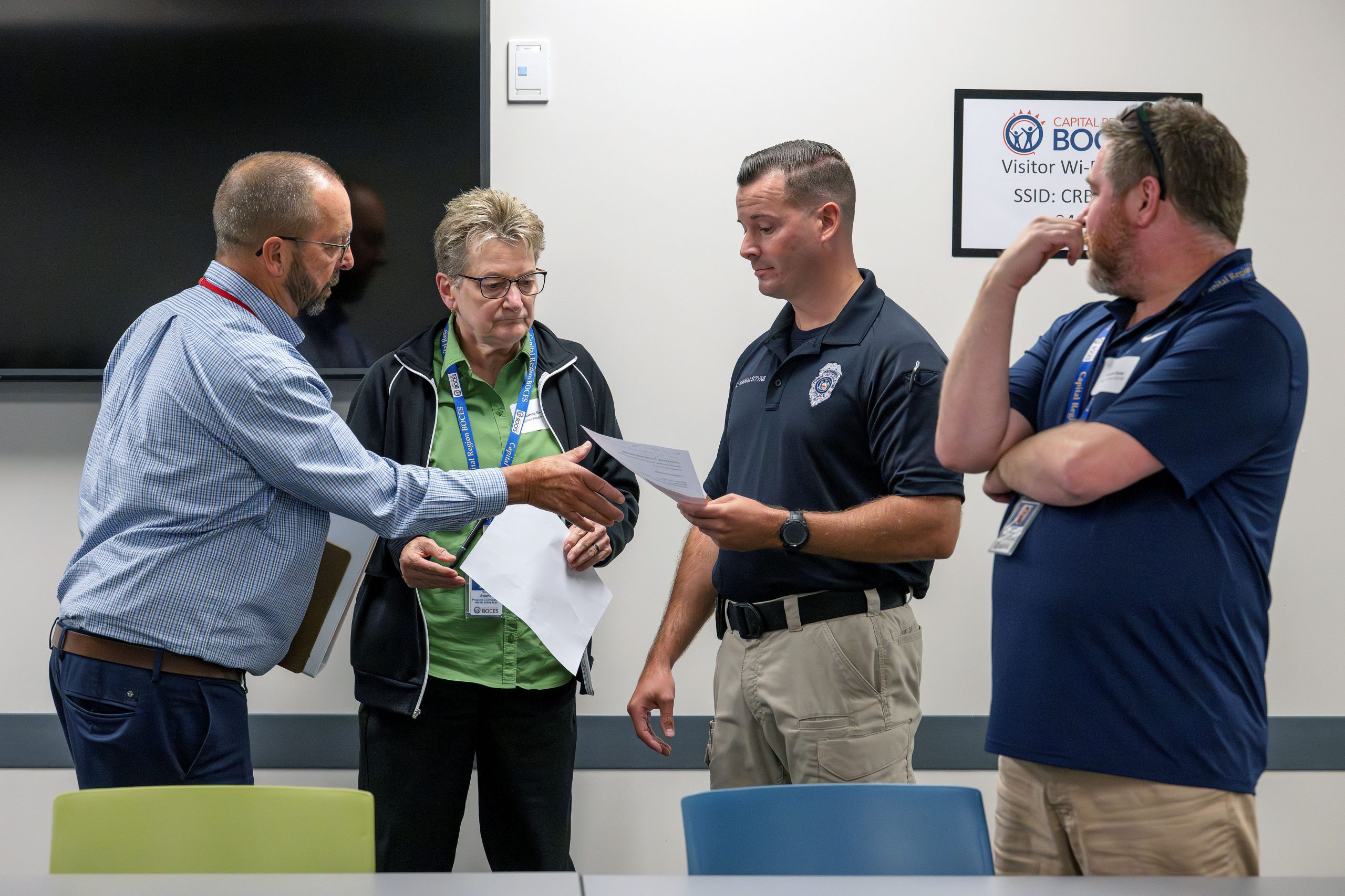 Four people are discussing something. One man is holding a piece of paper, one is gesturing