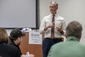 A man is standing in front of a conference room speaking