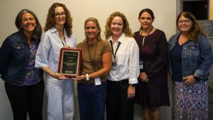 Six people are standing in a row. One is receiving a plaque