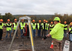 Students stand around a confined space as a person talks