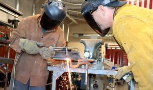 A student welds while a teacher watches