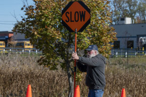 A participant in a flagger training is holding a sign that reads "slow" and his left arm is raised.