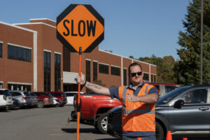 A participant in a flagger training is wearing a bright orange vest, holding an orange sign that says "slow." He is signaling with this left arm
