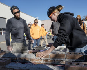 A student lays brick as a mason looks on