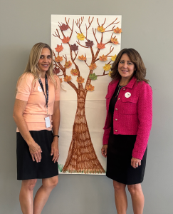 Two women standing with a poster drawing of a tree between them.