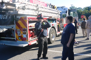 A Verdoy firefighter points to his shades while talking to a students as other students are seen waiting in line to get in the fire truck.
