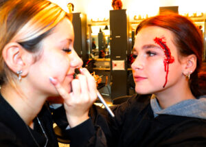 two students with fake scars put makeup on each other