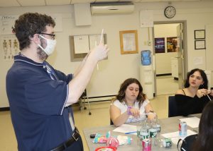 A teacher holds an item while two students look on